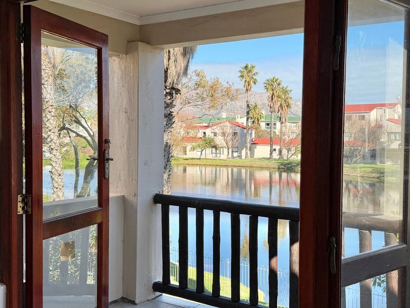A covered balcony featuring timber-framed glass doors and a wooden balustrade, offering scenic views over the estate lake and surrounding landscape.