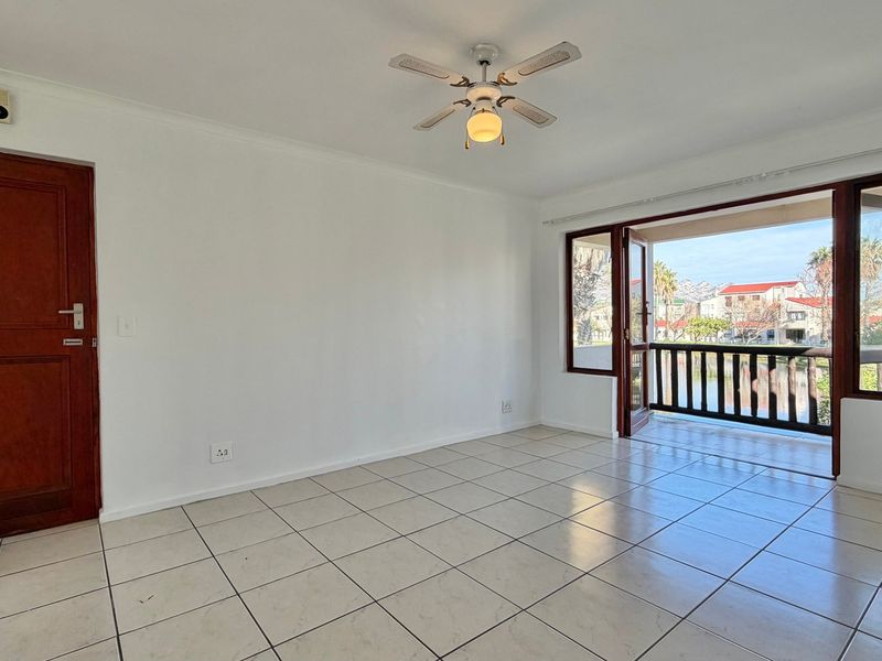 An empty living room featuring tiled flooring, a ceiling fan, and direct access to a balcony with exterior views.