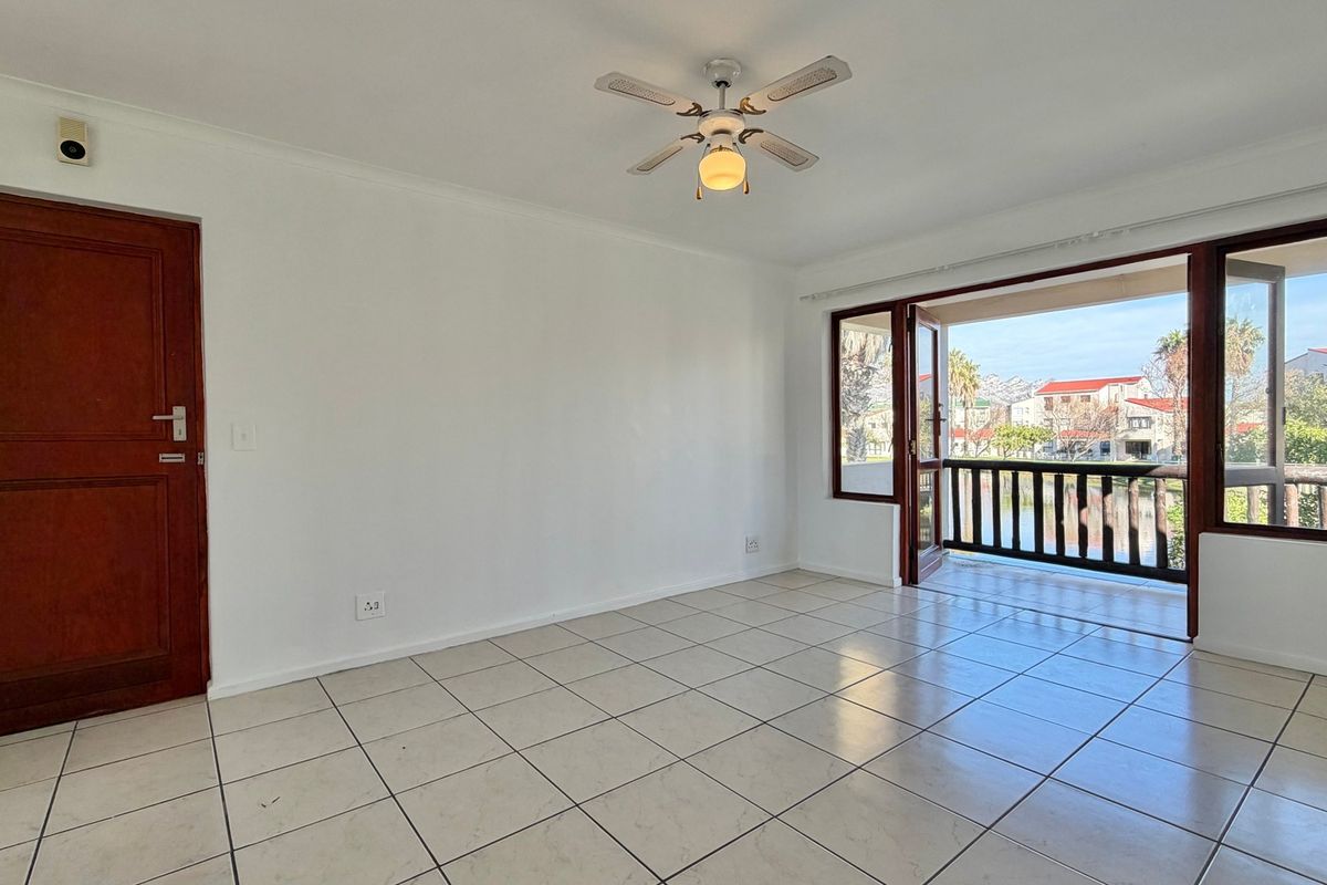 An empty living room featuring tiled flooring, a ceiling fan, and direct access to a balcony with exterior views.