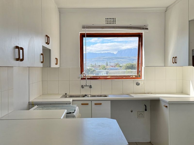 A functional kitchen featuring white cabinetry, a double basin sink, and a window offering scenic mountain views.