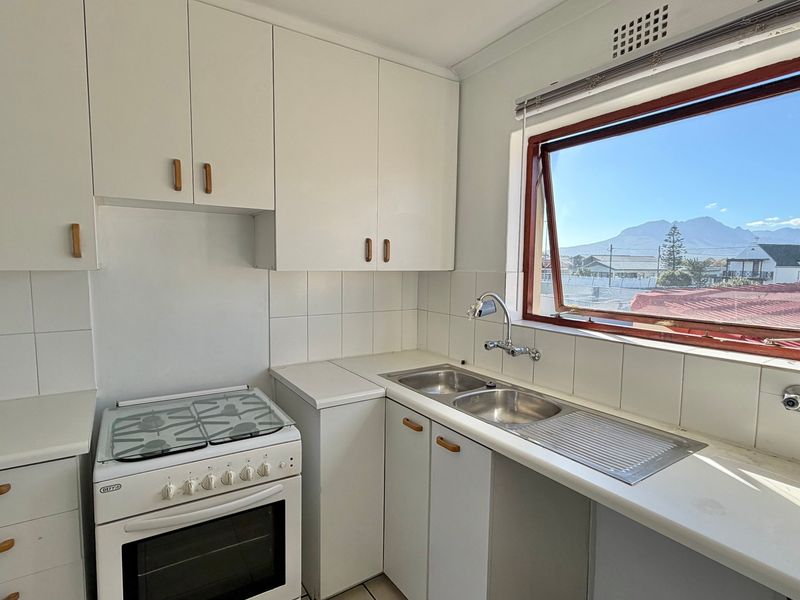 A functional kitchen featuring white cabinetry, a double sink, and a freestanding stove, complemented by a window offering scenic mountain views.