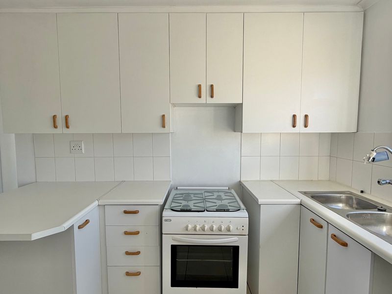 A functional kitchen featuring white built-in cabinetry, a freestanding stove, double bowl sink, and tiled splashback, offering a clean and practical workspace.