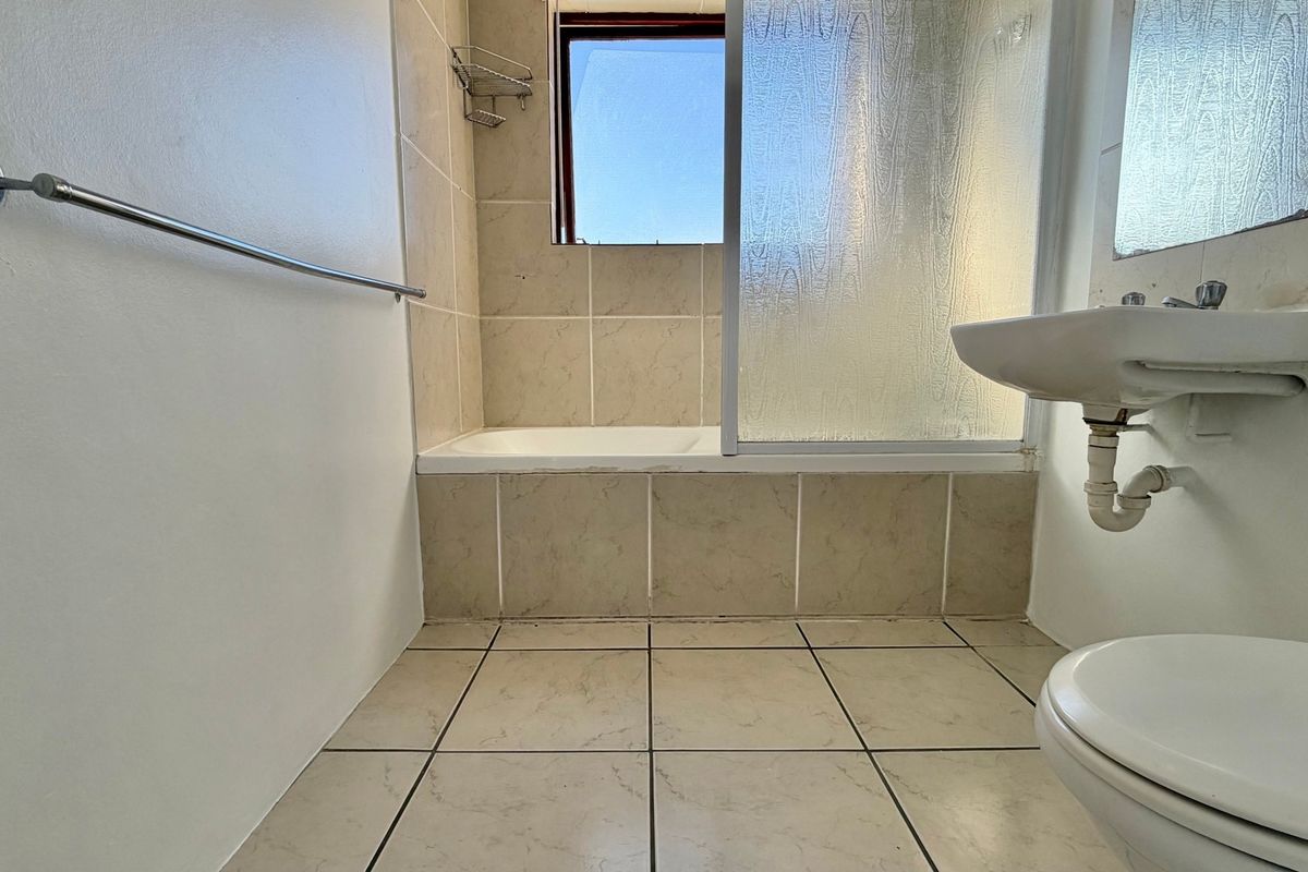 A functional bathroom featuring a bathtub with shower screen, pedestal basin, toilet, and neutral tiled finishes throughout.