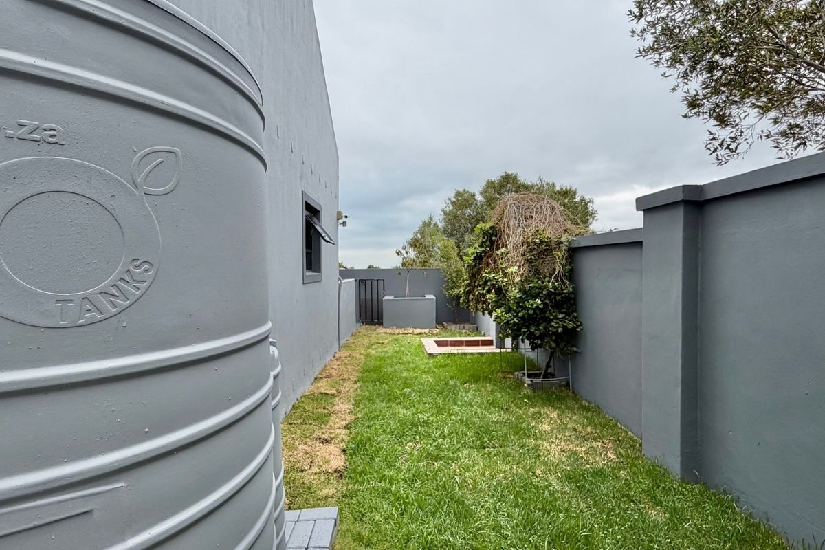 A side garden area featuring a large water storage tank, a well-maintained lawn, and high perimeter boundary walls.