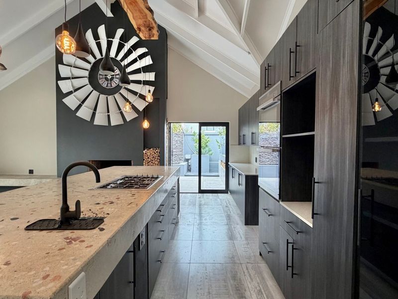 Modern open-plan kitchen and living area featuring a large stone island, gas hob, vaulted ceilings, and a feature fireplace with direct patio access.