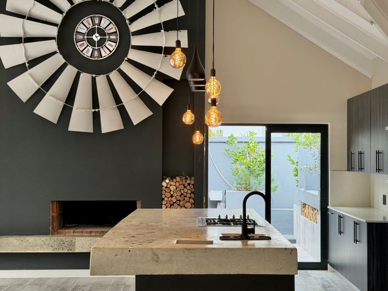 Modern open-plan kitchen and living area featuring a striking fireplace, stone island with integrated hob, and vaulted ceilings with direct patio access.