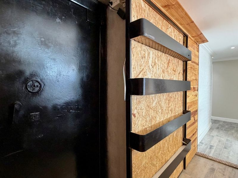 A utility area featuring a heavy-duty steel vault door, OSB wall paneling, and tiled flooring, currently presenting as an unfinished storage or secure space.