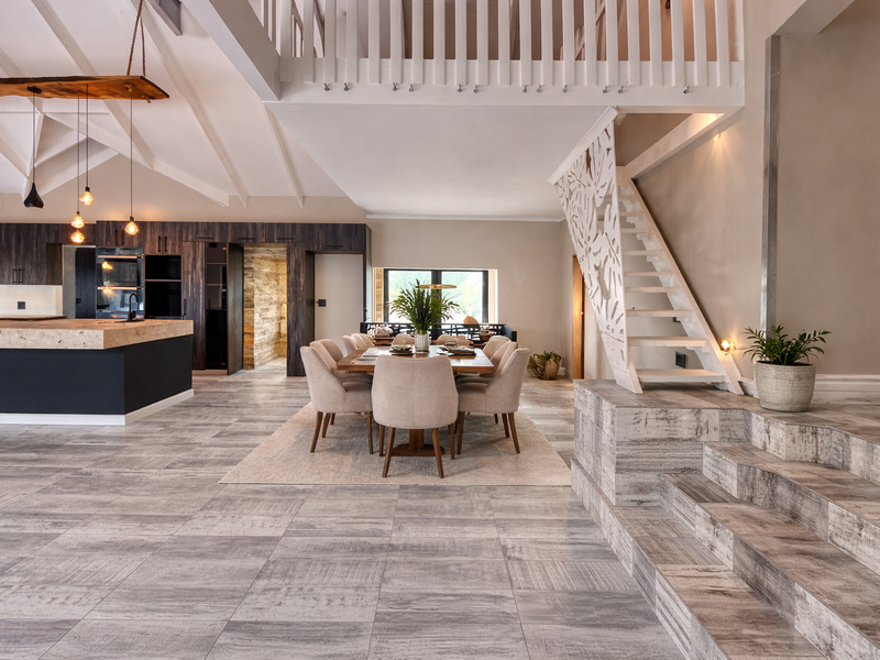 Spacious open-plan living area featuring a modern kitchen, dining space, vaulted ceilings, and a striking staircase leading to a mezzanine level.