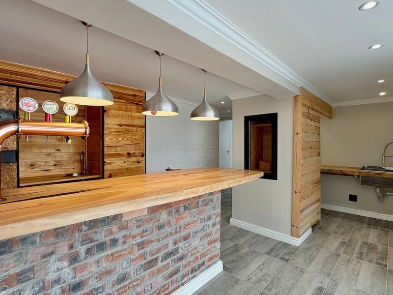 A modern, well-finished home bar area featuring a brick-base counter, timber accents, integrated beer taps, and a secondary sink area with tiled flooring.