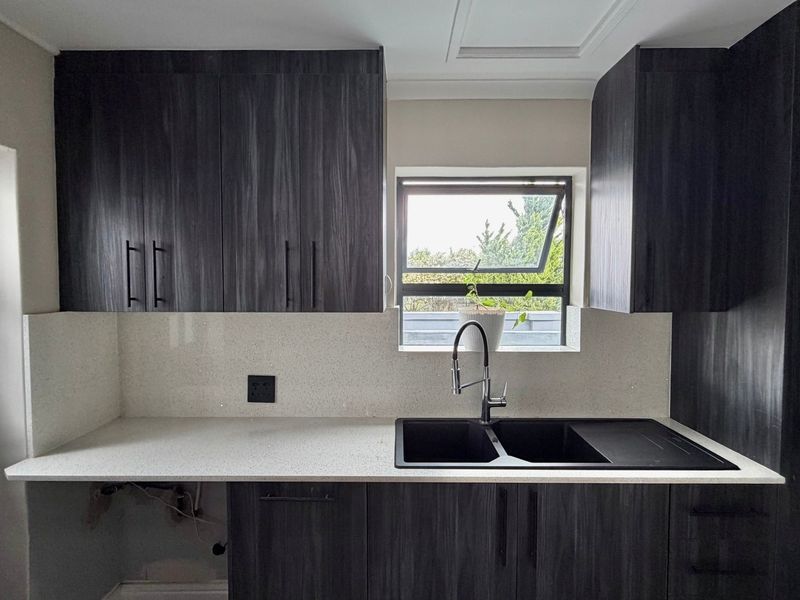 Modern kitchen area featuring dark wood cabinetry, stone countertops, and a double basin sink with a contemporary mixer tap.