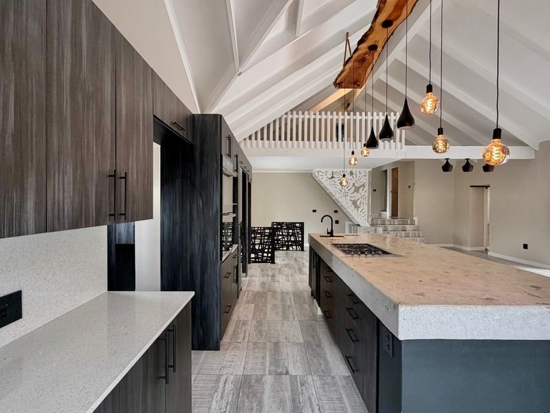 Modern open-plan kitchen featuring a large stone-topped island, dark cabinetry, exposed vaulted ceilings, and a mezzanine level overlooking the space.
