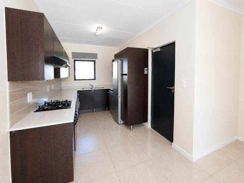 Modern kitchen featuring dark wood cabinetry, stone countertops, gas hob, extractor fan, and tiled flooring, offering a clean and functional workspace.