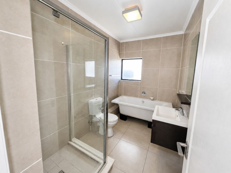 A modern, well-maintained bathroom featuring a glass shower enclosure, a freestanding bathtub, and a wall-mounted vanity with neutral tiling throughout.