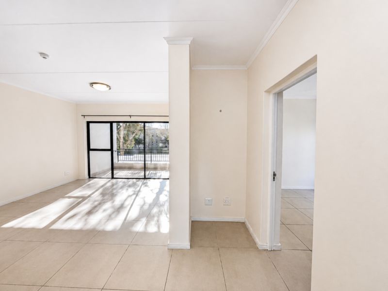 An empty, sunlit living area featuring neutral tiled flooring, coved ceilings, and a sliding glass door leading to an outdoor balcony.