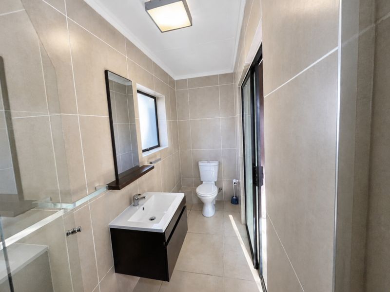 Modern bathroom featuring floor-to-ceiling neutral tiling, a wall-mounted vanity with basin, a toilet, and a glass-enclosed shower area.