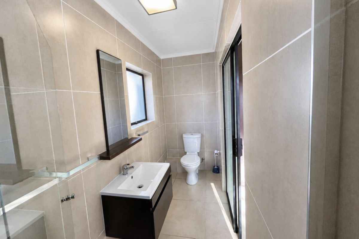 Modern bathroom featuring floor-to-ceiling neutral tiling, a wall-mounted vanity with basin, a toilet, and a glass-enclosed shower area.