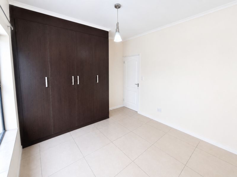 A bright, empty bedroom featuring large dark wood built-in cupboards, neutral tiled flooring, and a modern pendant light fixture.