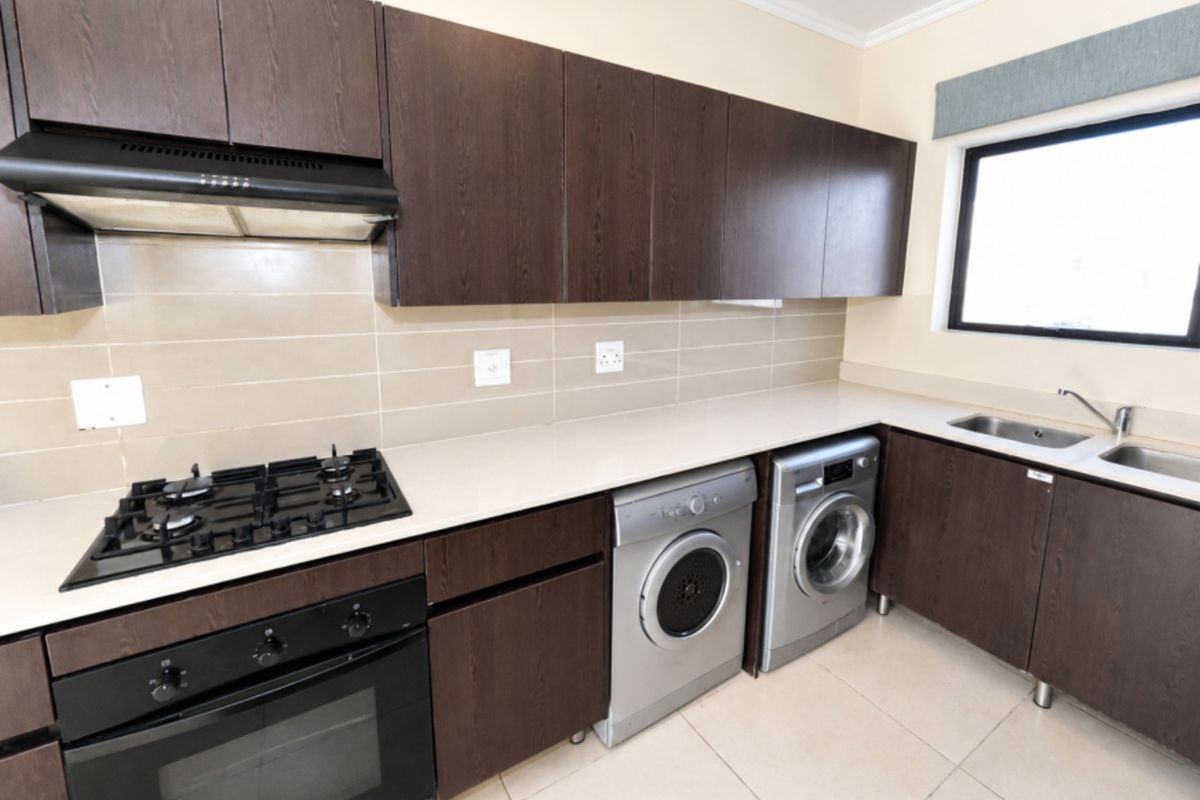 A functional kitchen featuring dark wood cabinetry, a gas hob, built-in oven, extractor fan, and integrated laundry appliance space with tiled flooring.