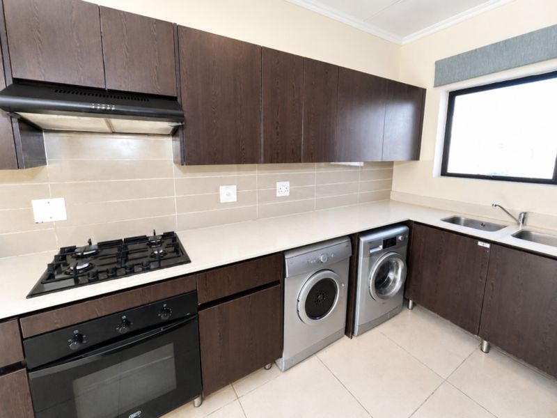 A functional kitchen featuring dark wood cabinetry, a gas hob, built-in oven, extractor fan, and integrated laundry appliance space with tiled flooring.
