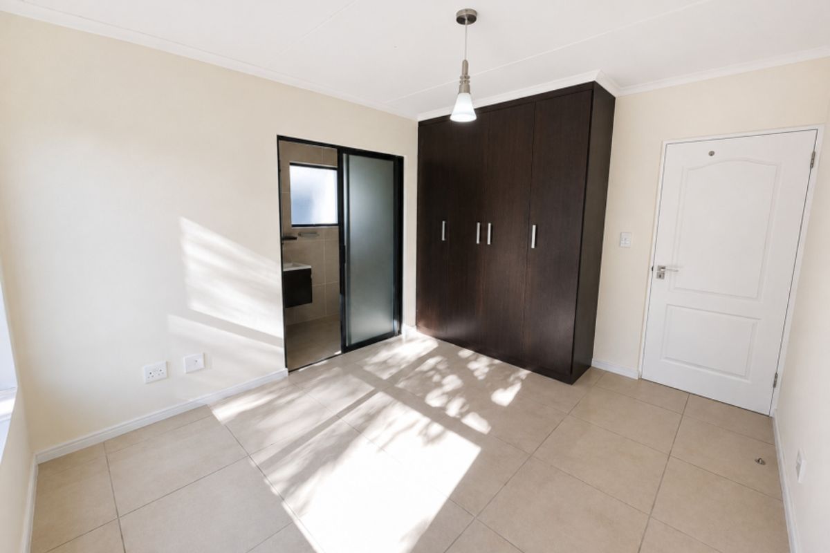 A bright, empty bedroom featuring neutral tiled flooring, dark wood built-in cupboards, and direct access to an en-suite bathroom.