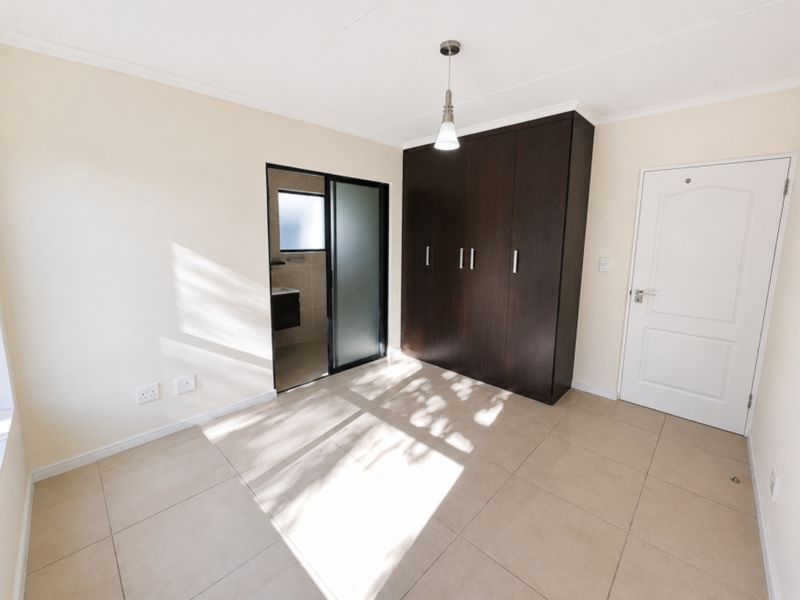 A bright, empty bedroom featuring neutral tiled flooring, dark wood built-in cupboards, and direct access to an en-suite bathroom.