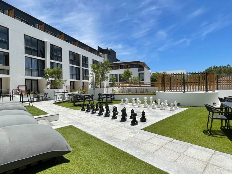 A well-maintained communal outdoor courtyard featuring paved areas, artificial grass, and recreational space with modern apartment building architecture in the background.