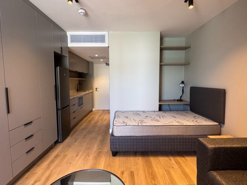 Modern open-plan studio apartment featuring sleek built-in cabinetry, integrated kitchen facilities, ducted air conditioning, and high-quality laminate flooring throughout.