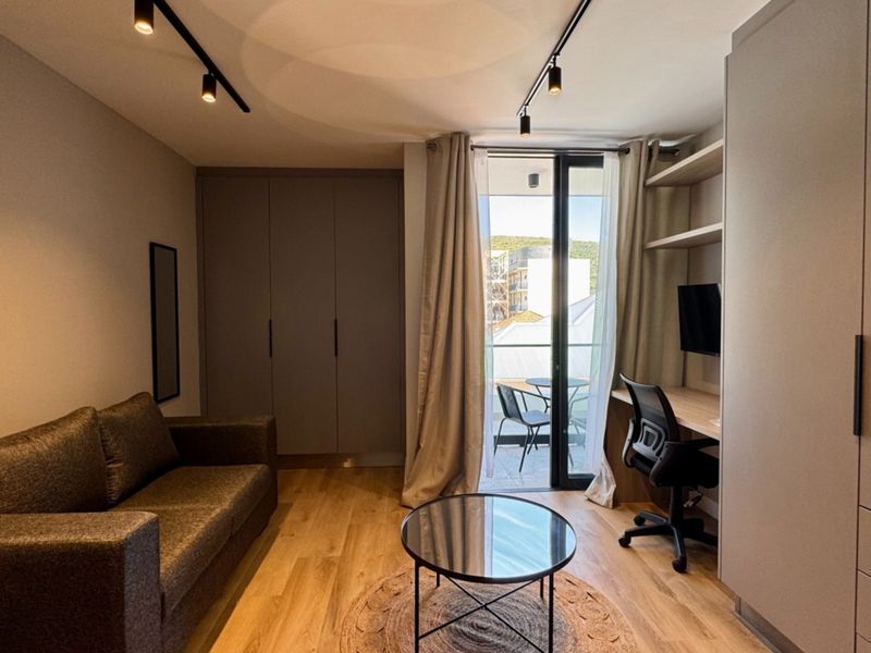 Modern living room featuring built-in cabinetry, a dedicated workspace, track lighting, and direct access to a private balcony.