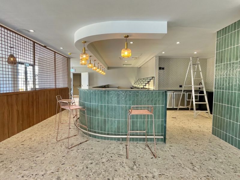 A modern, stylish bar area featuring a curved green tiled counter, terrazzo flooring, and decorative pendant lighting, creating a sophisticated social space.