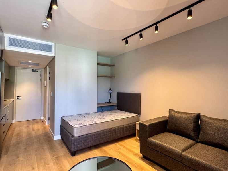 Modern open-plan studio apartment featuring sleek built-in cabinetry, track lighting, ducted air conditioning, and durable laminate flooring in a well-maintained contemporary space.