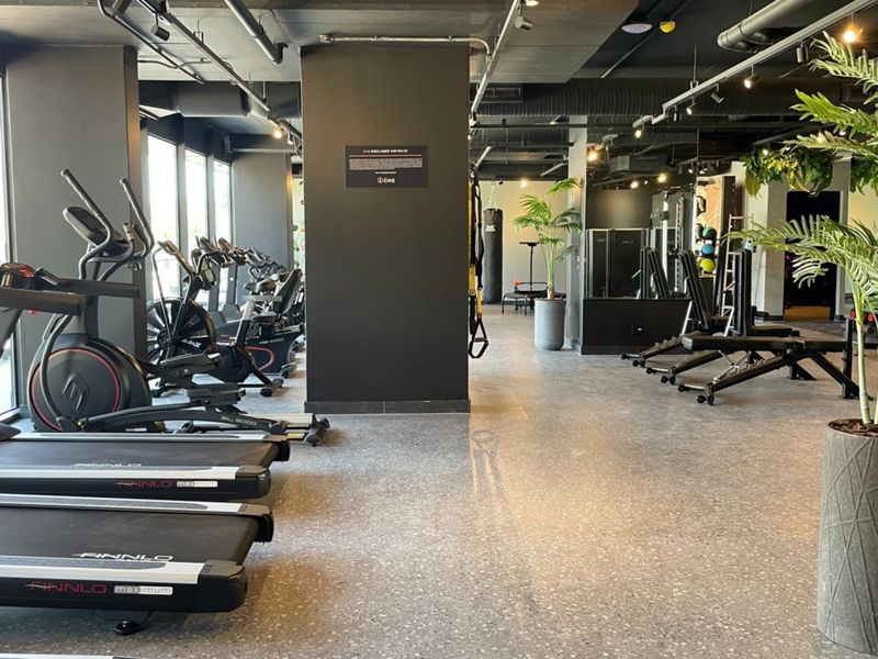 A modern, well-maintained apartment complex gym featuring industrial-style exposed ceilings, terrazzo flooring, and a variety of professional fitness equipment.