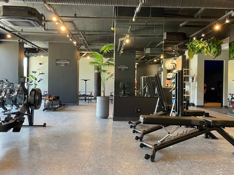 A modern, well-equipped apartment gym featuring industrial-style exposed ceilings, mirrored walls, and high-quality vinyl flooring with professional lighting.