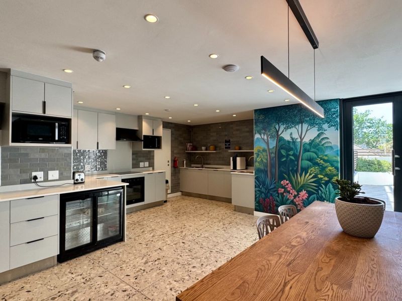Modern open-plan kitchen featuring sleek cabinetry, integrated appliances, terrazzo flooring, and direct access to an outdoor area through glass doors.