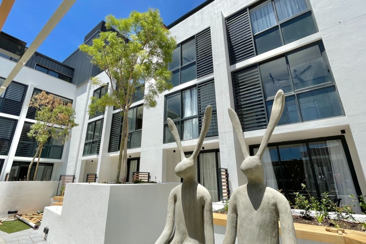 Modern multi-story apartment complex exterior featuring clean white facades, large glass sliding doors, integrated louvre shutters, and a landscaped courtyard area.