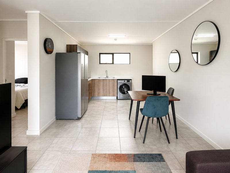 Open-plan living and kitchen area featuring neutral tiled flooring, modern cabinetry, and integrated laundry facilities in a well-maintained apartment setting.