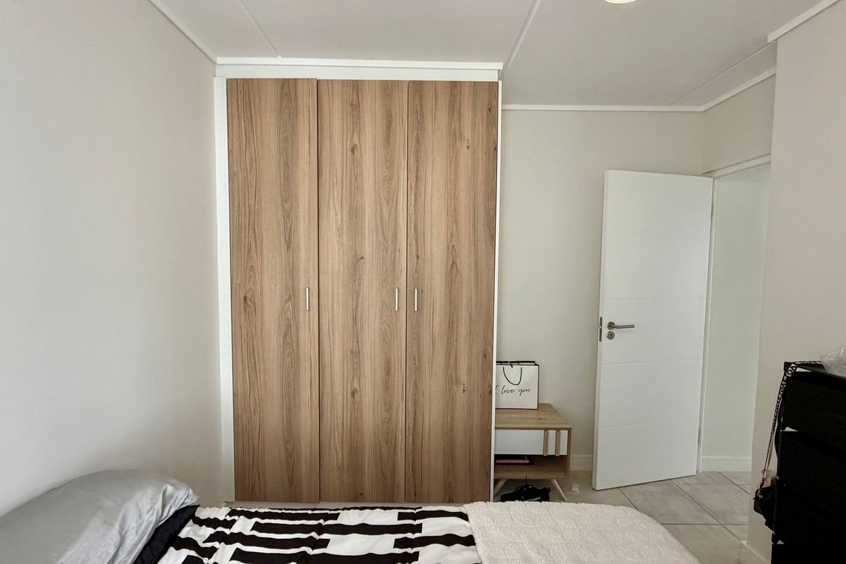 A well-maintained bedroom featuring modern wood-finish built-in wardrobes and neutral wall tones.
