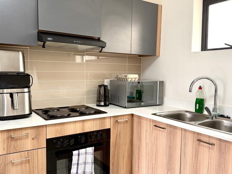 Modern kitchen featuring wood-finish cabinetry, quartz countertops, a tiled backsplash, and integrated appliances including an electric hob, oven, and extractor fan.
