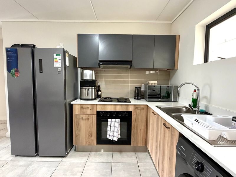Modern kitchen featuring wood-grain and grey cabinetry, built-in oven and hob, tiled backsplash, and double sink with tiled flooring.