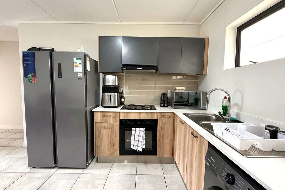 Modern kitchen featuring wood-grain and grey cabinetry, built-in oven and hob, tiled backsplash, and double sink with tiled flooring.