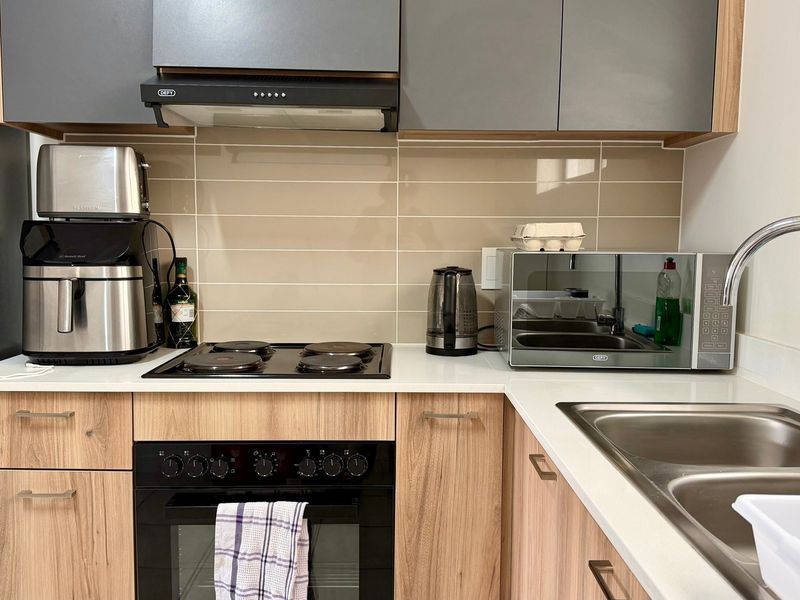 Modern kitchen featuring wood-grain cabinetry, stone countertops, a built-in oven with electric hob, extractor fan, and a stainless steel double sink.