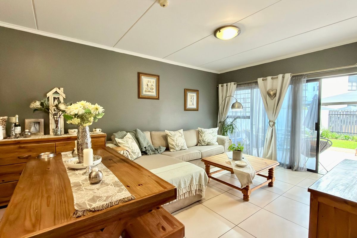 A well-maintained living room featuring neutral tiled flooring and a large sliding glass door providing access to the outdoor patio area.