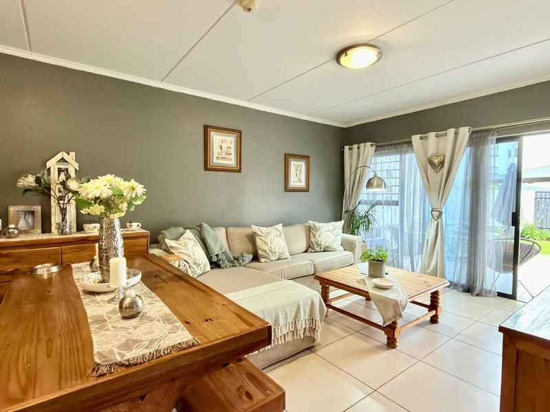 A well-maintained living room featuring neutral tiled flooring and a large sliding glass door providing access to the outdoor patio area.