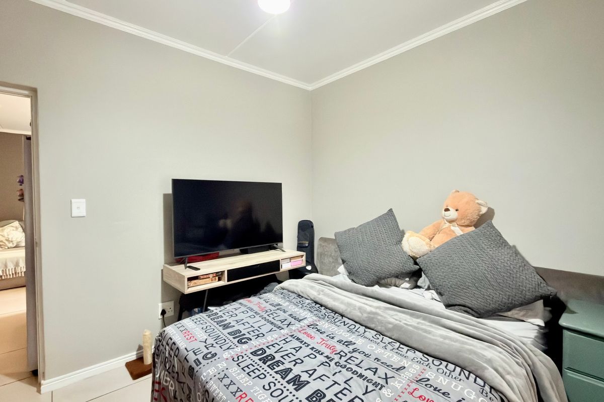 A bedroom featuring neutral wall paint, crown molding, and a wall-mounted media shelf, with an adjacent view into another room.