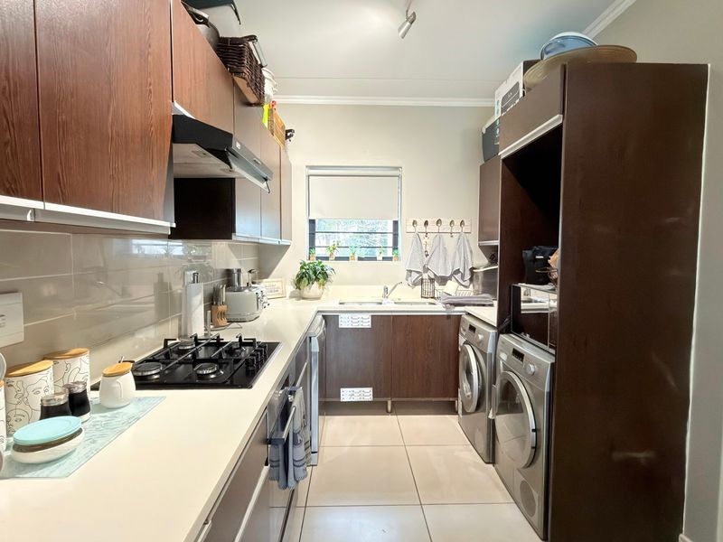 Compact galley-style kitchen featuring dark wood cabinetry, stone countertops, a gas hob with extractor, and integrated space for laundry appliances.