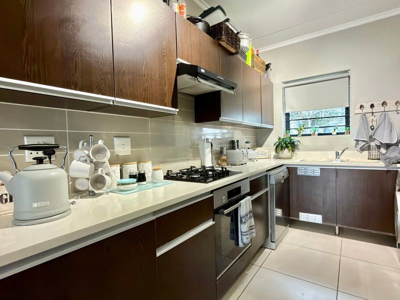 Modern kitchen featuring dark wood cabinetry, stone countertops, integrated gas hob, built-in oven, and tiled flooring with a functional layout.