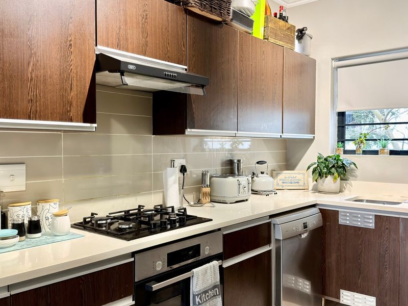 A well-maintained kitchen featuring dark wood cabinetry, stone countertops, a gas hob, built-in oven, and a stainless steel sink with a window view.