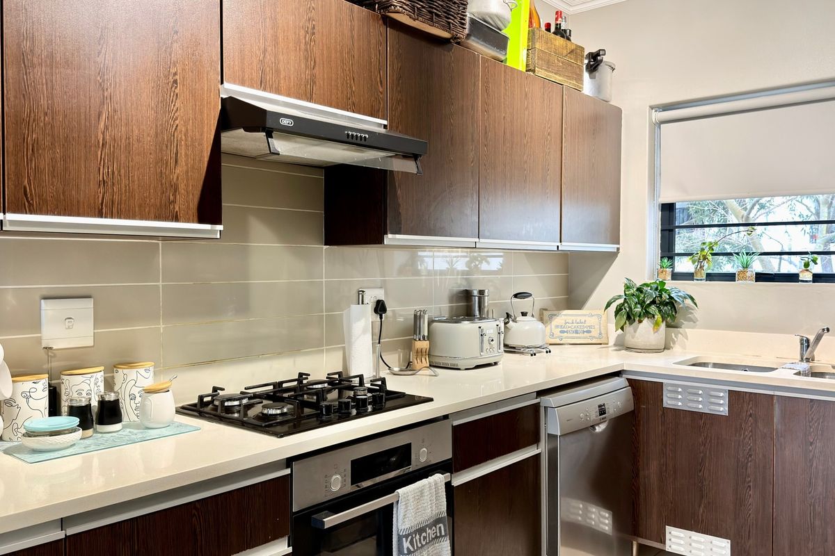 A well-maintained kitchen featuring dark wood cabinetry, stone countertops, a gas hob, built-in oven, and a stainless steel sink with a window view.