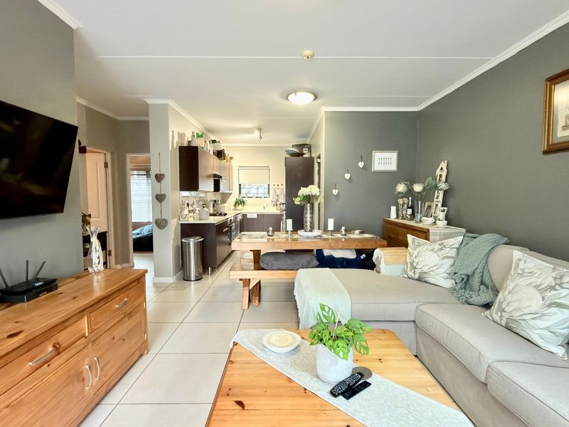An open-plan living and dining area featuring tiled flooring and a connected kitchen with dark cabinetry, creating a functional and cohesive living space.