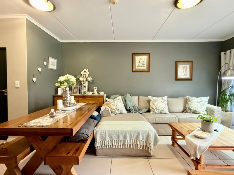 A well-maintained open-plan living and dining area featuring neutral tiled flooring, modern grey accent walls, and direct access to a balcony through sliding doors.