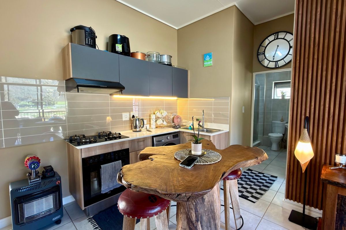 Modern compact kitchen featuring sleek grey cabinetry, gas hob, integrated oven, tiled backsplash, and a stylish slatted wood feature wall.